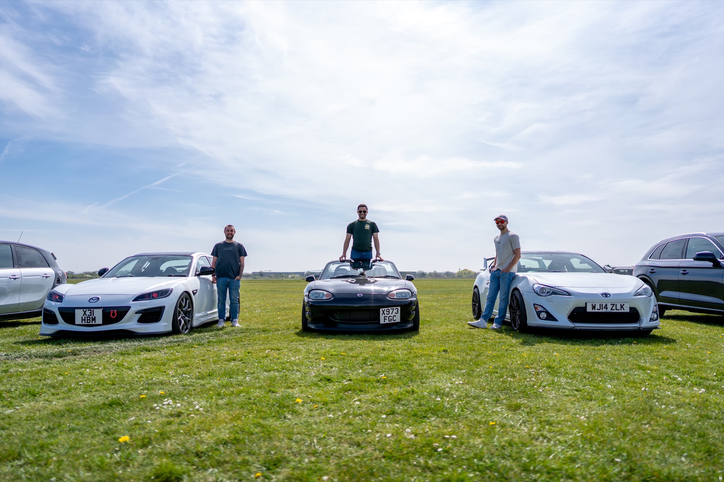 Harry, Aaron and Tom, the RevBase Automotive team, with their Mazda RX-8, Mazda MX-5 and Toyota GT86 on a grass airfield
